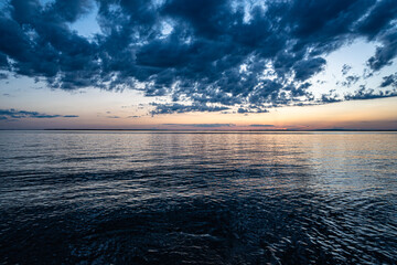 Tranquil sunset over Lake Saint-Louis in Quebec with dramatic clouds and calm water reflecting the fading light. Peaceful nature moment captured at dusk.