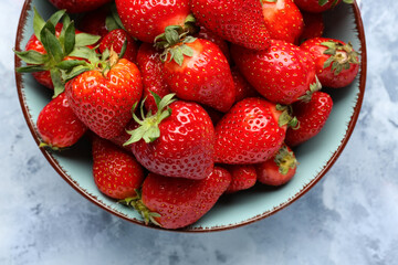 Bowl with fresh strawberries on blue background