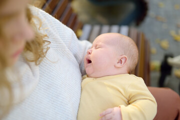 Sweet 2 month old infant lying in mommy's arms. Hungry or tired baby screams loudly. Mother consoling her crying newborn baby. Portrait of beautiful newborn girl baby.