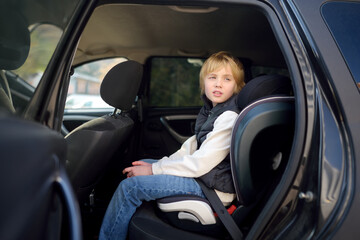 Preteen boy is sitting in the backseat of a car wearing a seat belt in a child safety seat. Safety of transportation of children.