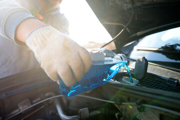 Man auto mechanic pours the liquid for washing the windows of the car