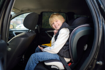 Preteen boy is sitting in the backseat of a car wearing a seat belt in a child safety seat. Safety of transportation of children.