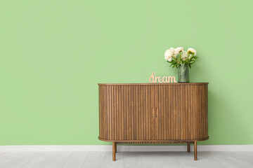 Vase of white peonies and decor in shape of word DREAM on dresser near green wall