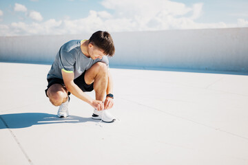 Focused runner ties shoelaces on a bright morning in an urban setting with beautiful skies