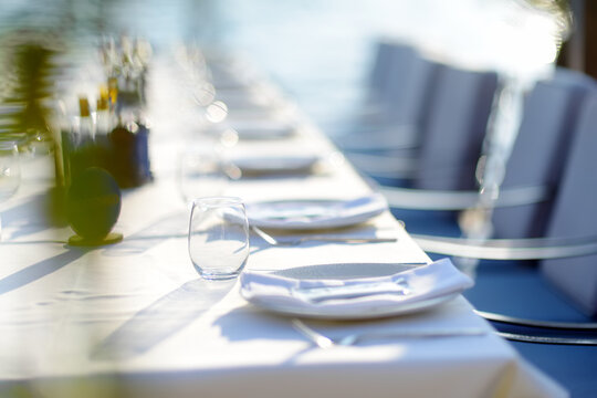 A row of empty plates on a long table with a white tablecloth. A table in a Mediterranean restaurant ready to serve a large group of visitors or tourists.