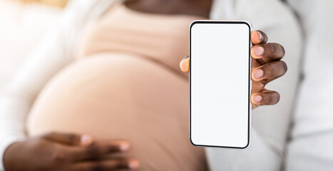 Pregnancy App. Black pregnant lady demonstrating smartphone with blank white screen, recommending new app for expecting women, demonstrating maternity shopping website, mockup image with copy space