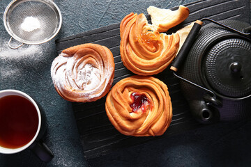 Wooden board with tasty cruffins and cup of tea on black background