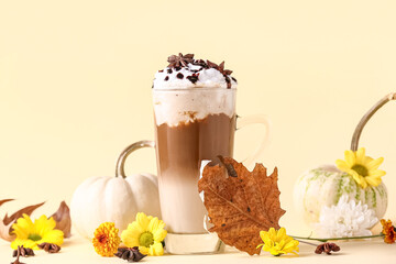 Glass cup of tasty pumpkin latte with star anise and beautiful flowers on yellow background