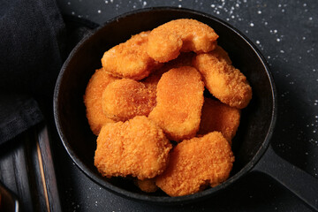Frying pan with tasty nuggets on black background
