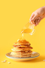 Woman pouring sweet honey onto tasty pumpkin pancakes on yellow background
