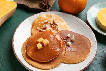 Plate of tasty pumpkin pancakes with honey and nuts on green background