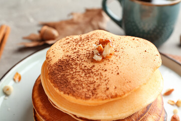 Plate of tasty pumpkin pancakes with cocoa powder and nuts on grey background