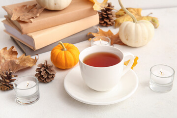 Cup of tea, books, autumn leaves, burning candles, pine cones and pumpkins on white background