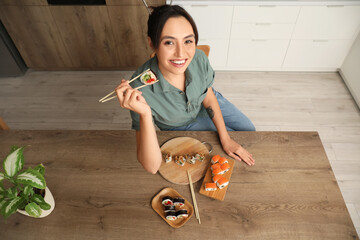 Happy young woman eating tasty sushi rolls at home