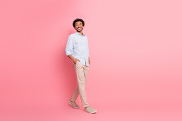 Smiling young man in casual striped shirt and trousers in front of pink background exuding confidence and charm