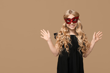 Happy little girl wearing carnival mask on beige background
