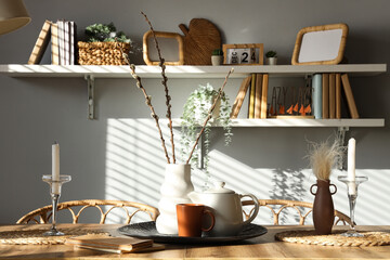Vase with willow branches, teapot and cup on dining table in room