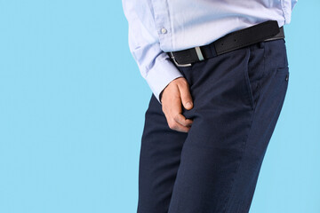Young businessman with prostate problem on blue background, closeup. Cancer awareness concept