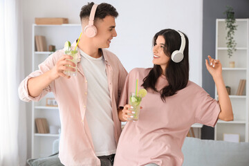 Happy young couple in headphones with glasses of mojito at home