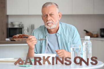 Senior man suffering from Parkinson syndrome eating at table in kitchen
