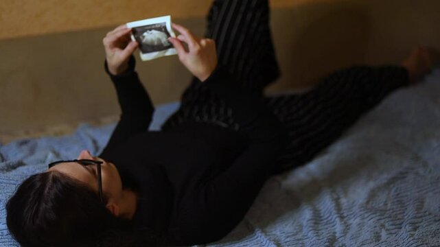 a young woman lying on the couch looks at an ultrasound scan for pregnancy