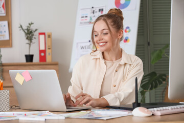 Female web designer working with laptop at table in office