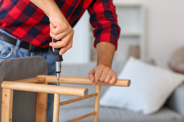 Young man with screwdriver assembling soft bench at home, closeup