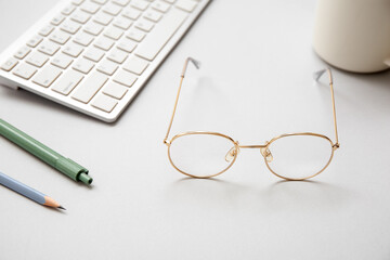 Stylish eyeglasses, computer keyboard, pen and pencil on grey background