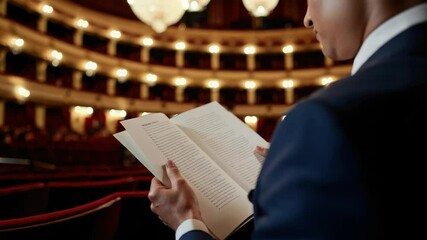 Person in formal attire reading program at elegant theater