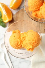 Balls of tasty orange sorbet in dessert bowls, fresh fruit and mint on white marble table, flat lay