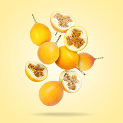 Delicious ripe passion fruits falling on pale yellow gradient background