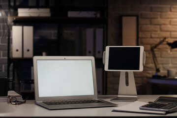 Fototapeta premium Blank laptop with tablet computer on desk in office at night