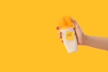 Obraz premium Woman holding bottle of sunscreen cream and sticky note with word SPF on yellow background
