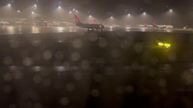 Rain drops on plane window in Brisbane International Airport runway at night.Modern aircraft will take off and land in the rain regardless of the heaviness of the rain.