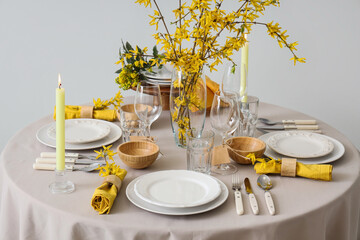 Elegant table setting with clean plates, burning candles, cutlery and blooming tree branches