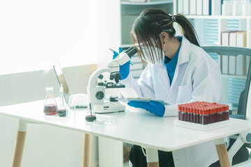 Fototapeta premium Researcher's hand holding blood vessel. Examination of blood vessel in research laboratory. Blood sample wearing blue rubber gloves in laboratory and holding blood sample with microscope next to it.