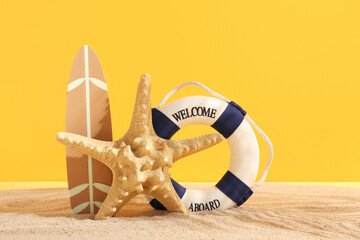 Lifebuoy ring with surfboard and starfish on sand against orange background