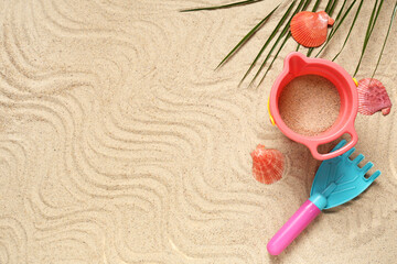 Composition with seashells, palm leaf, toy rake and bucket on sand as background