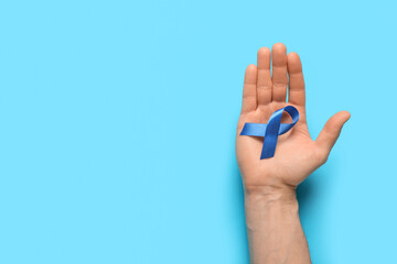 Male hand holding blue ribbon on color background. Prostate cancer awareness concept
