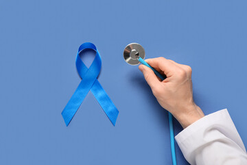 Male doctor's hand with blue ribbon and stethoscope on color background. Prostate cancer awareness...