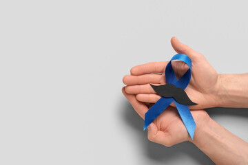 Male hands with blue ribbon on grey background. Prostate cancer awareness concept