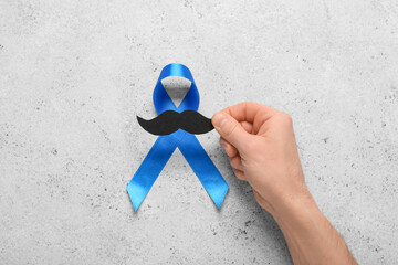 Male hand with blue ribbon and paper mustache on grey grunge background. Prostate cancer awareness...