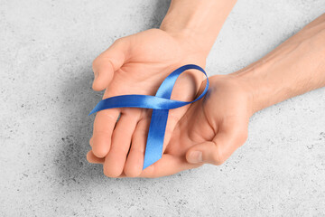 Male hands with blue ribbon on grey grunge background. Prostate cancer awareness concept