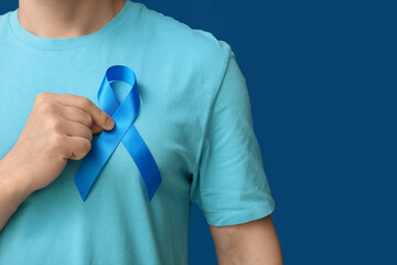 Young man holding blue ribbon on color background. Prostate cancer awareness concept
