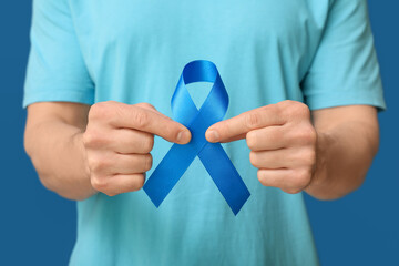 Young man holding blue ribbon on color background. Prostate cancer awareness concept