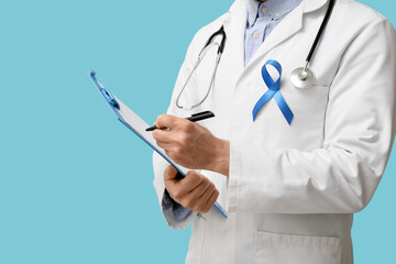 Male doctor with clipboard and blue ribbon on color background. Prostate cancer awareness concept