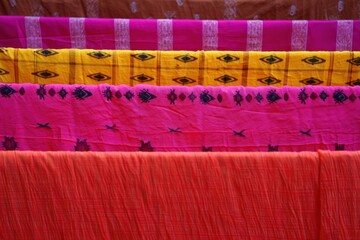 Brightly colored patterned fabrics hung in parallel rows showcasing vibrant orange, pink, yellow, and magenta hues with intricate decorative motifs and textures
