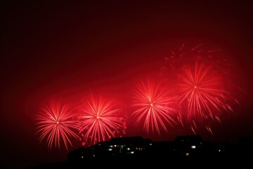 Bright red fireworks bursting in the night sky above dark silhouetted buildings with illuminated windows creating a festive atmosphere