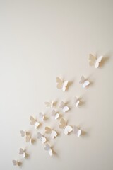 Group of delicate white paper butterflies arranged artistically on a soft beige wall creating a sense of lightness and gentle movement