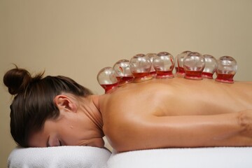 Woman lying face down with glass cupping therapy cups on her back in a calm indoor setting